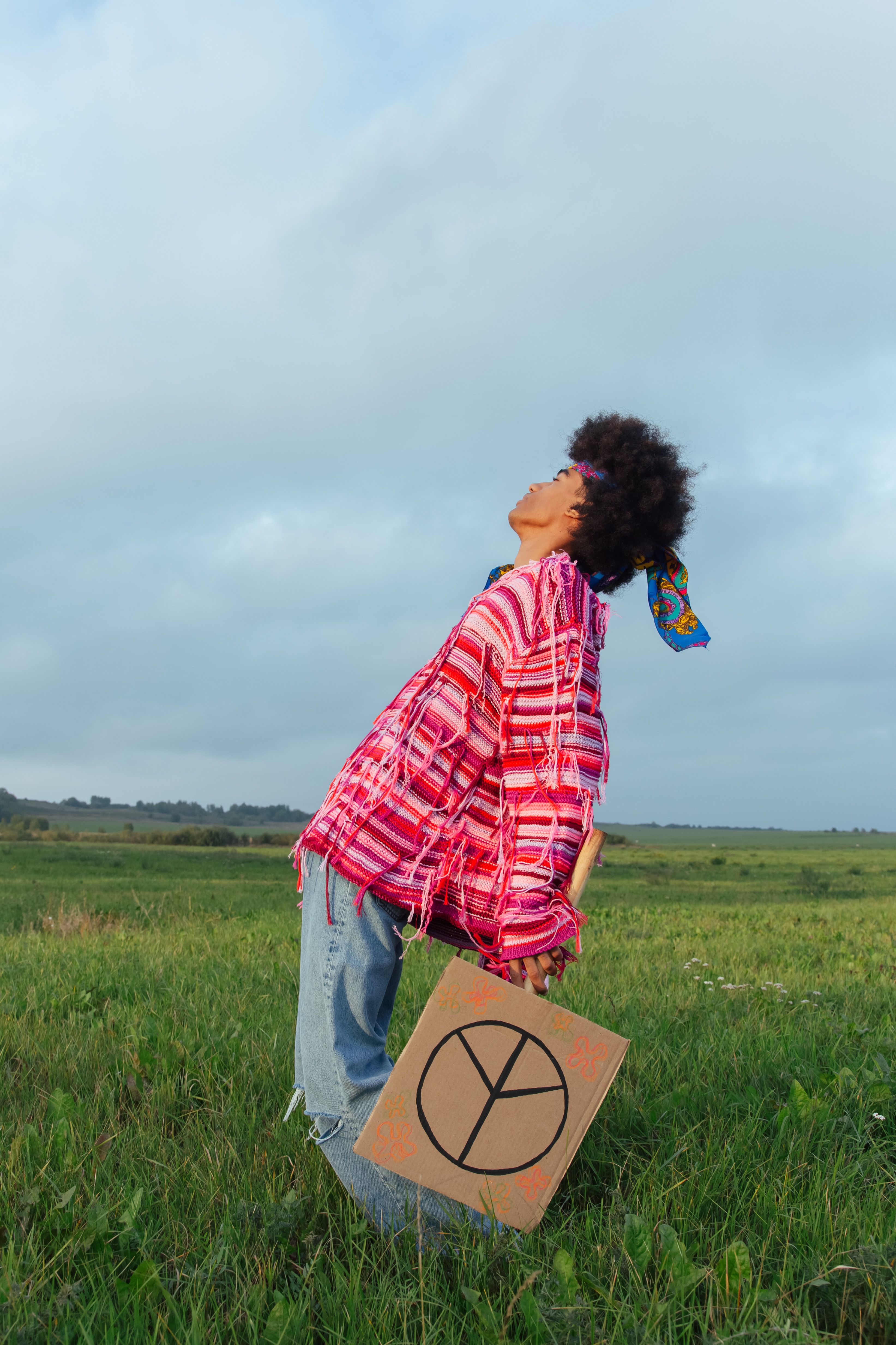An African adult holds a peace placard in a green field wearing vibrant clothing.