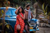 一对时尚的年轻夫妇在户外自然环境中，对着一辆老爷车摆出姿势，散发着充满活力的现代生活气息