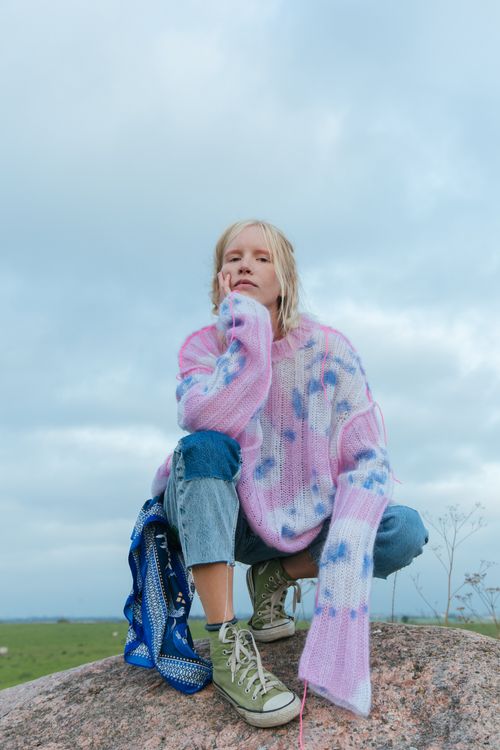 Free A young woman in a vibrant sweater poses on a rock in a natural setting. Stock Photo
