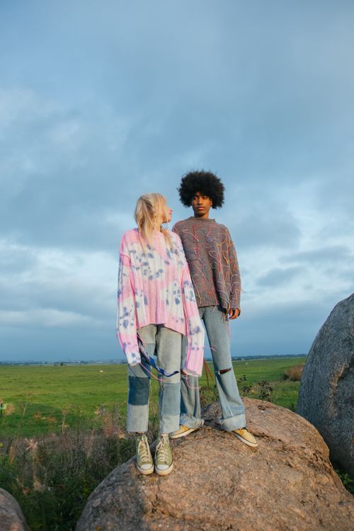 Free Young couple in trendy outfits standing on rocks in an open field under a cloudy sky. Stock Photo