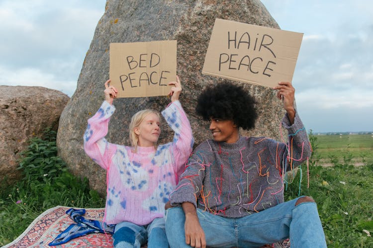 Couple Sitting Together Near The Huge Boulder While Holding Signages About Peace