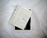 A White Earphones Lying on a Book Over a White iPad