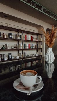 Warm, inviting cafe interior featuring a latte on table with modern decor and shelves.