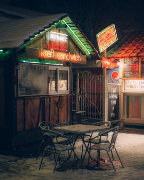 Neon-lit food stall with chairs and tables on a snowy winter night.