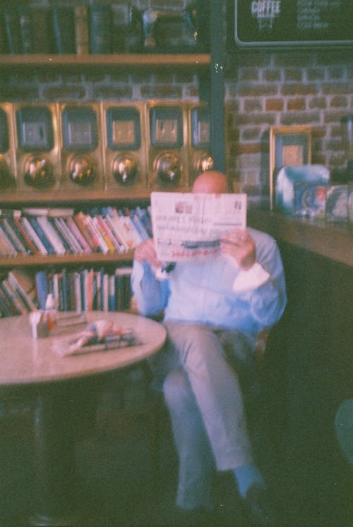 A Person Sitting at the Table Reading Newspaper
