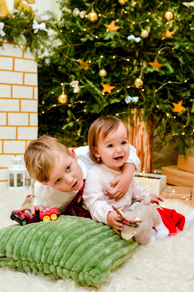 A Boy Hugging A Crying Girl Sitting Near A Christmas Tree