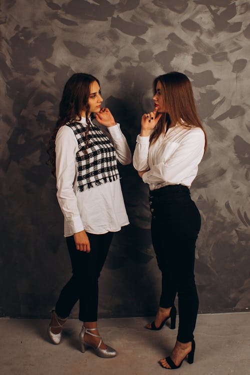 Free Women in Long Sleeve Shirts and Black Pants Standing Facing Each Other Stock Photo