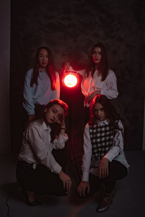 Free Four women posing artistically with a central red light creating a moody atmosphere. Stock Photo