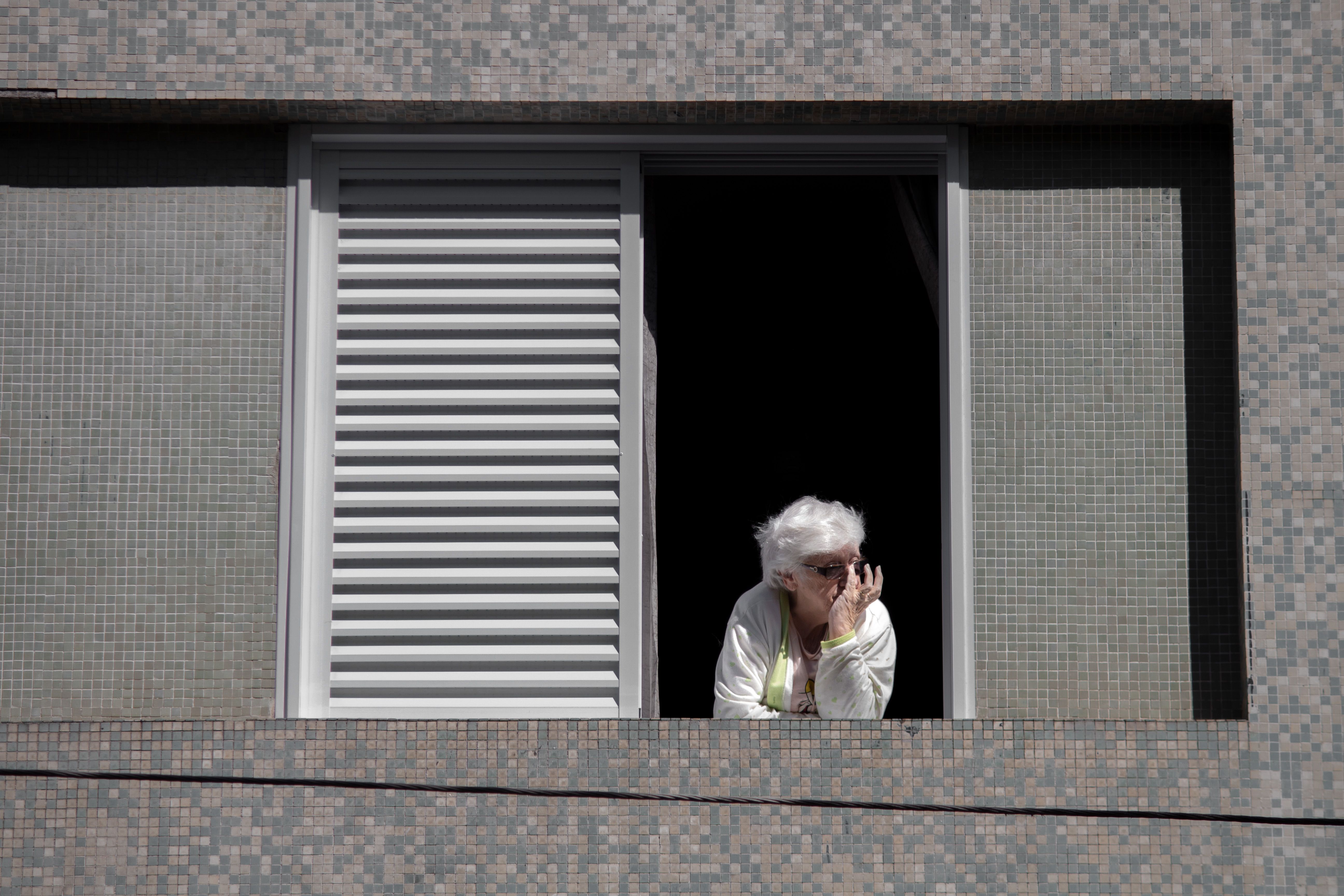 Elderly Spanish woman standing outside apartment building with worried expression after eviction