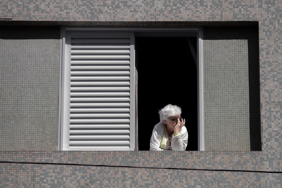 Elderly Spanish woman standing outside apartment building with worried expression after eviction