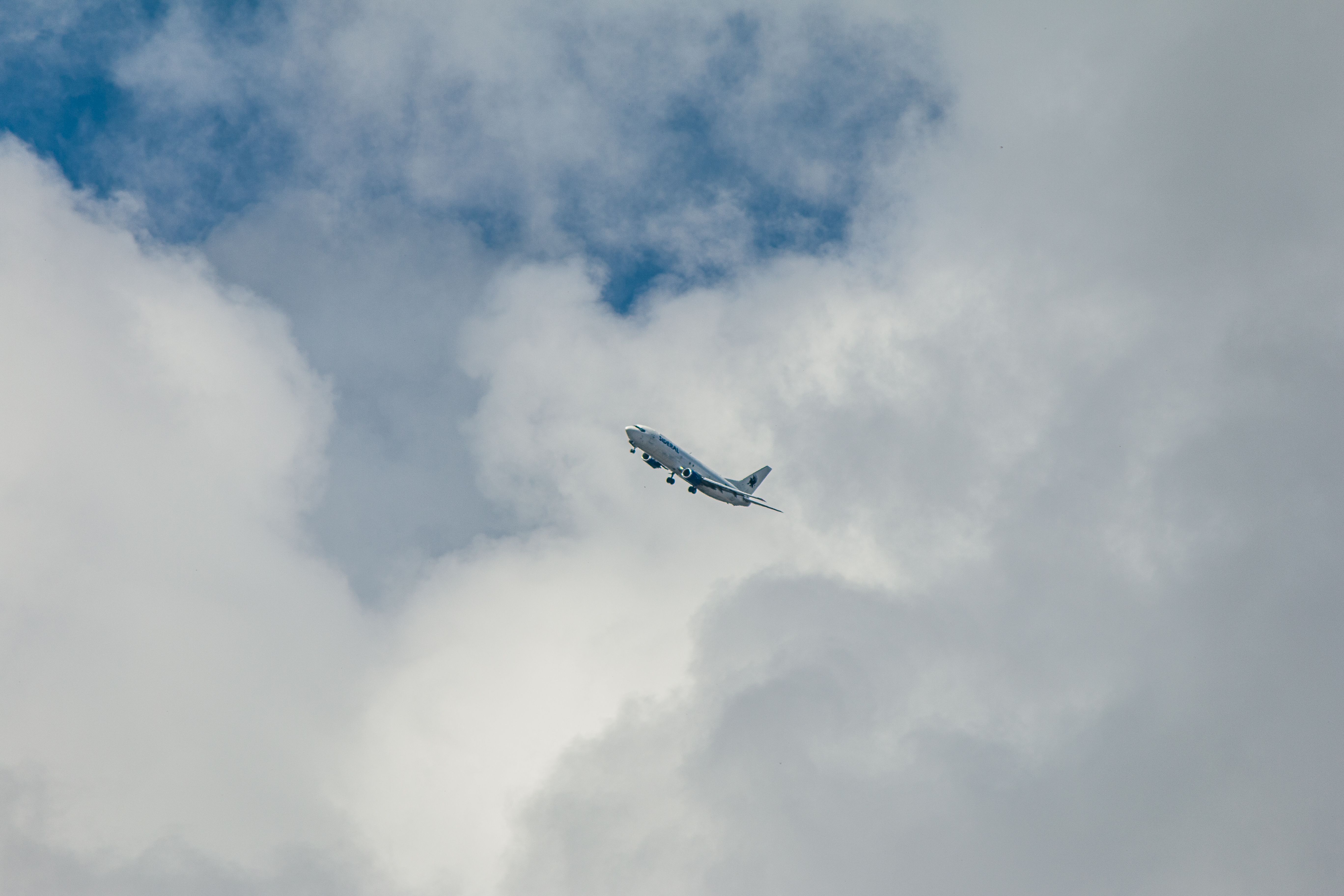 A large commercial airplane navigating through white fluffy clouds against a blue sky.