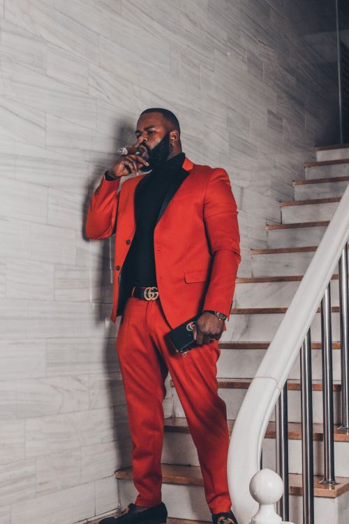 Free A fashionable adult man in a red suit stands smoking by stairs indoors, showcasing style and elegance. Stock Photo