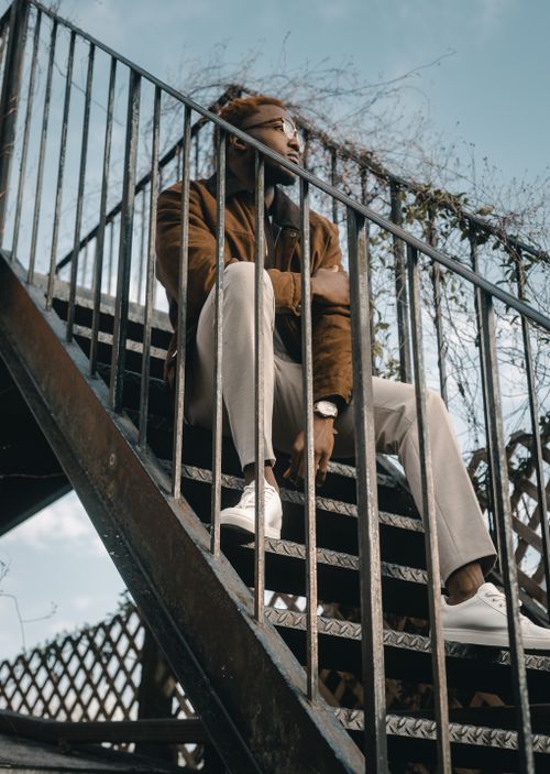 Free A fashionable man sitting on an outdoor staircase looks contemplative. Perfect for lifestyle and fashion themes. Stock Photo