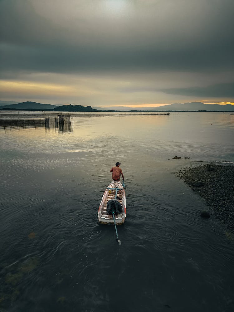 Man On Wooden Boat In Water On Sunset