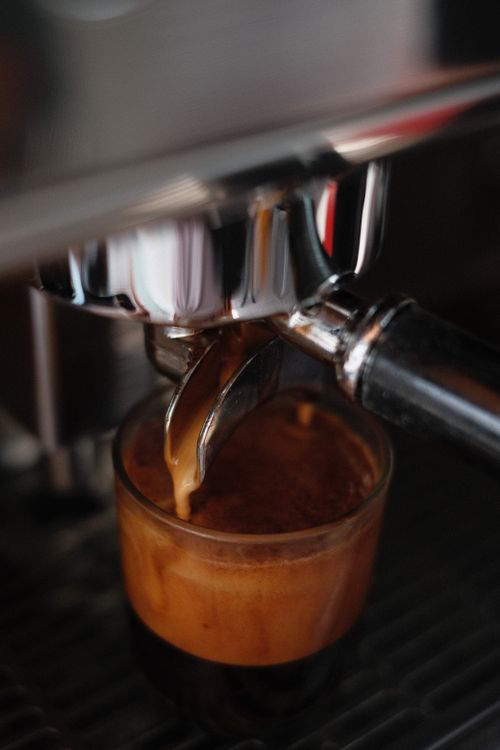 Free Espresso shot being poured from a coffee machine into a glass, capturing rich crema. Stock Photo