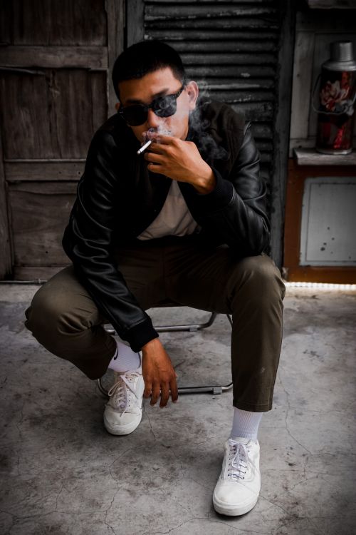 Free Stylish young man in a black leather jacket smoking outside, exuding a cool and relaxed vibe. Stock Photo