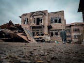 Man Walking by Damaged Building and Car