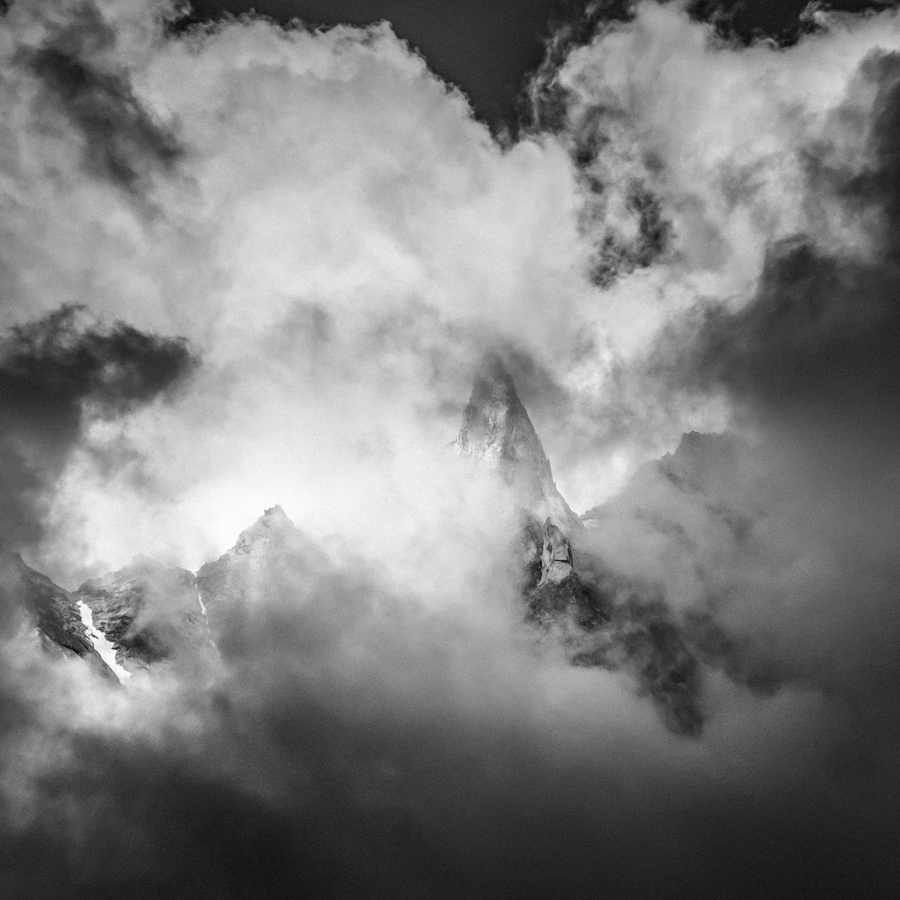 A captivating black and white photograph of mountain peaks surrounded by dramatic clouds.