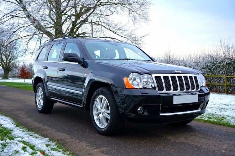 Black Jeep Suv On Black Asphalt Road Near On Snowy Grass Lawn