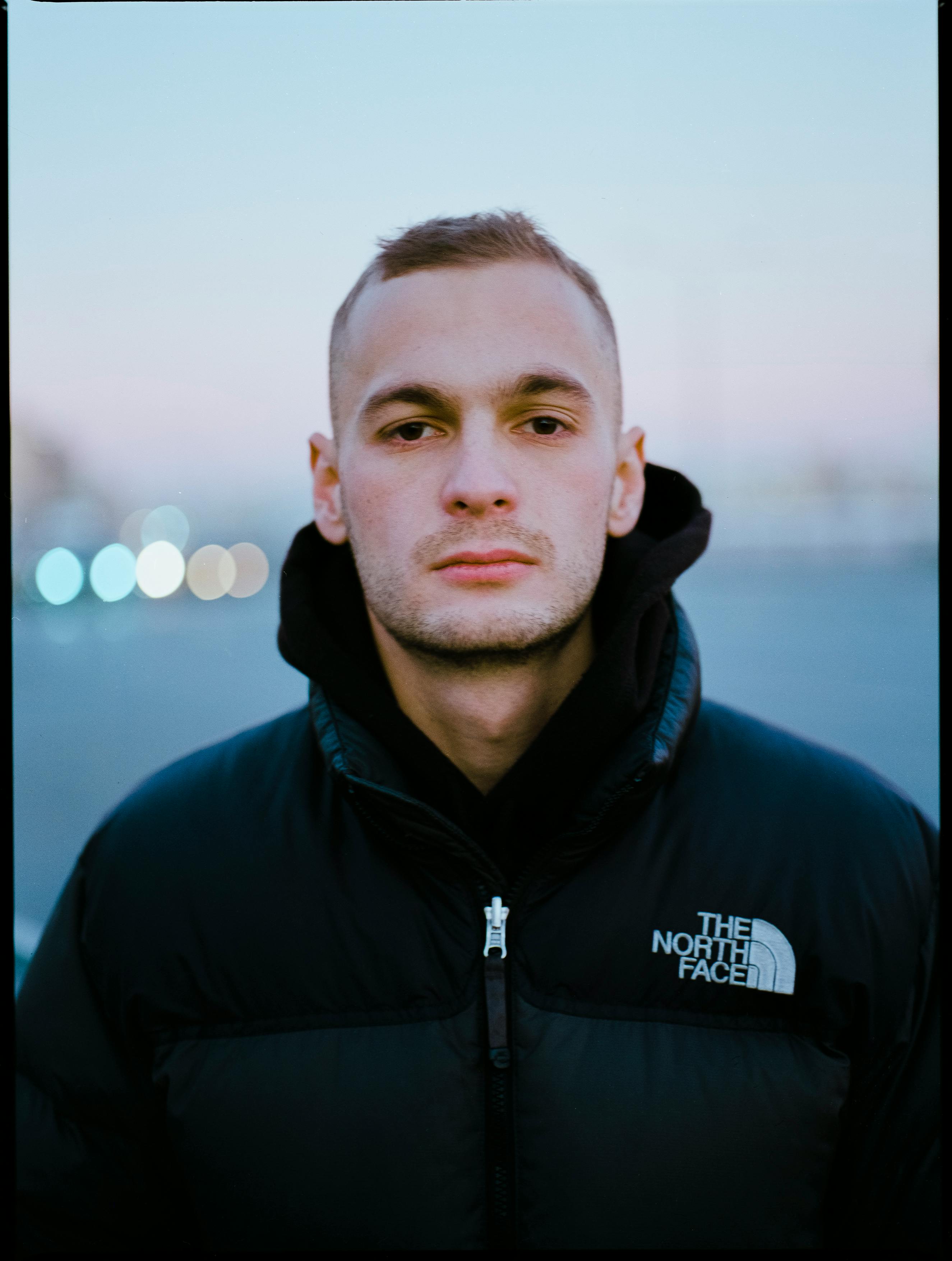 Close-up portrait of a man wearing a winter jacket, set against a blurry outdoor background at twilight in Saint Petersburg.