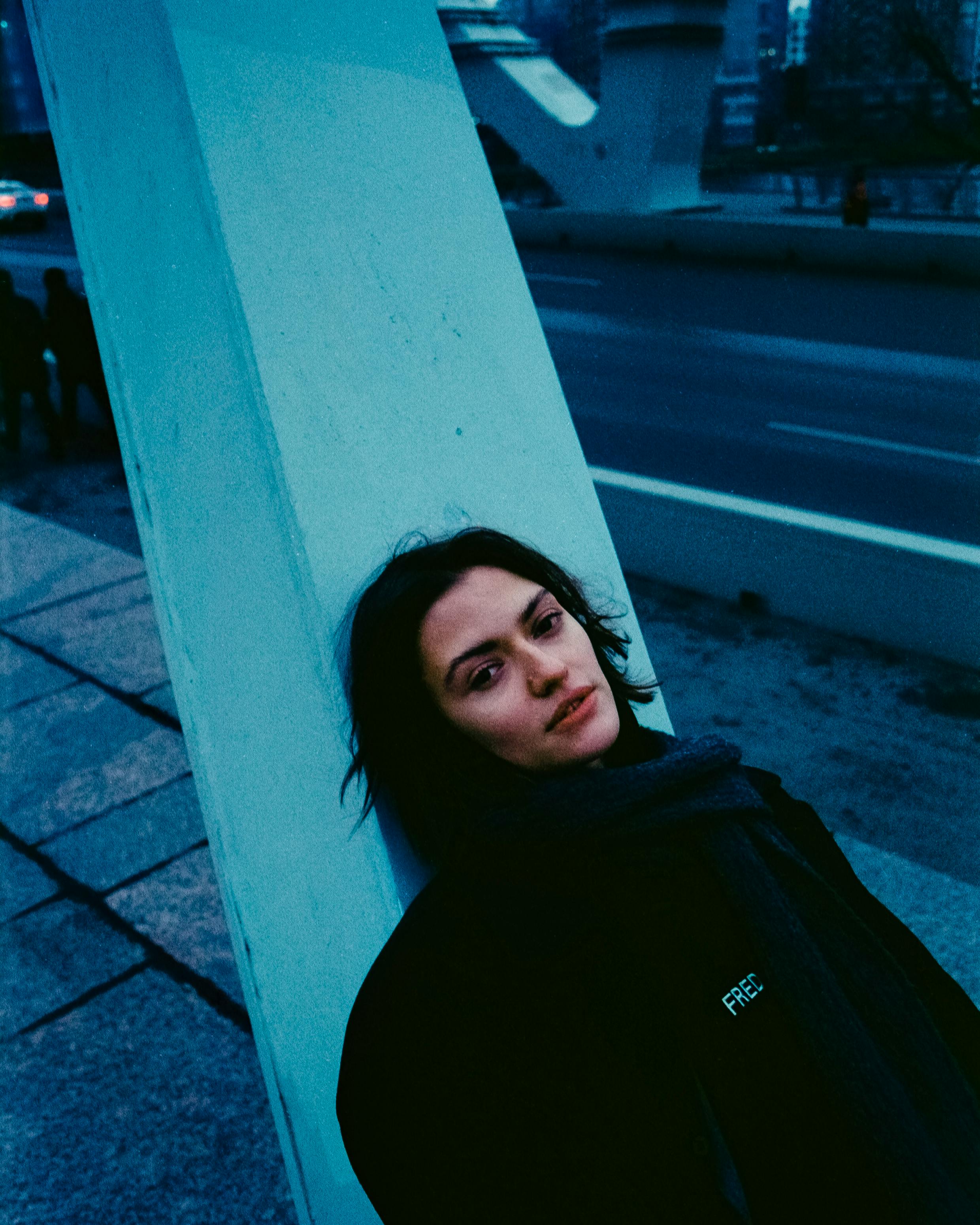 A woman in dark clothing leans against a column in a Saint Petersburg street, capturing a moody urban moment.