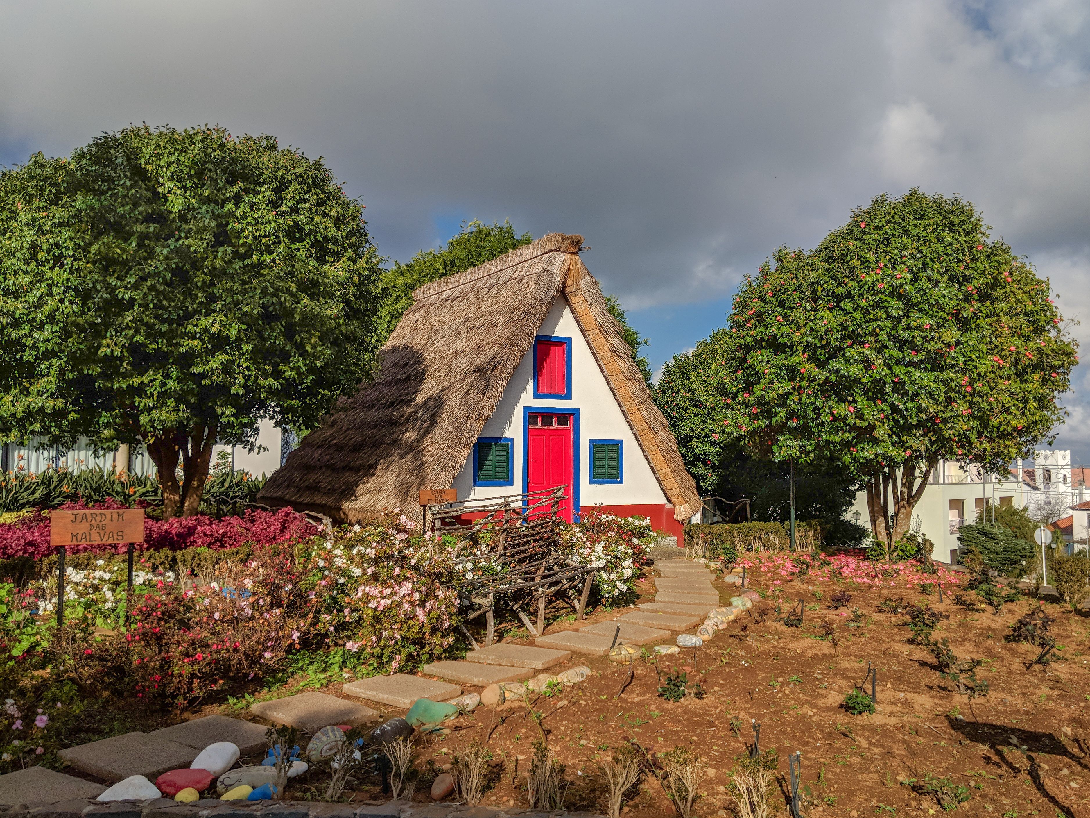 A vibrant A-frame thatched house in sunny Santana, Madeira with lush gardens.