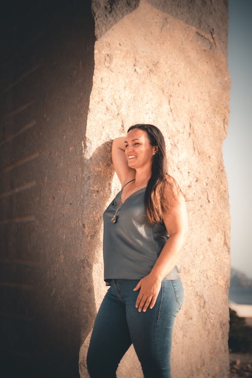 A Portrait of a Woman in a Spaghetti Strap Top and Denim Pants Leaning on a Wall