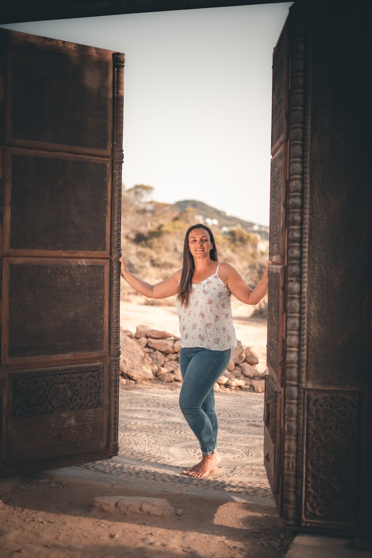 A Woman In A Spaghetti Strap Top And Denim Pants Opening A Door