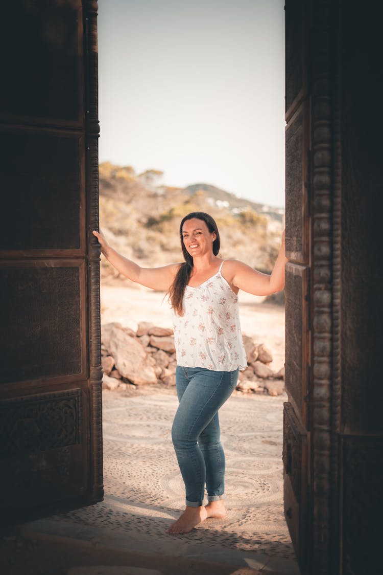 A Woman In A Spaghetti Strap Top And Denim Pants Opening A Door