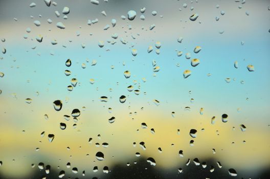Water droplets on glass with a blurred landscape background, capturing ambient light effects.