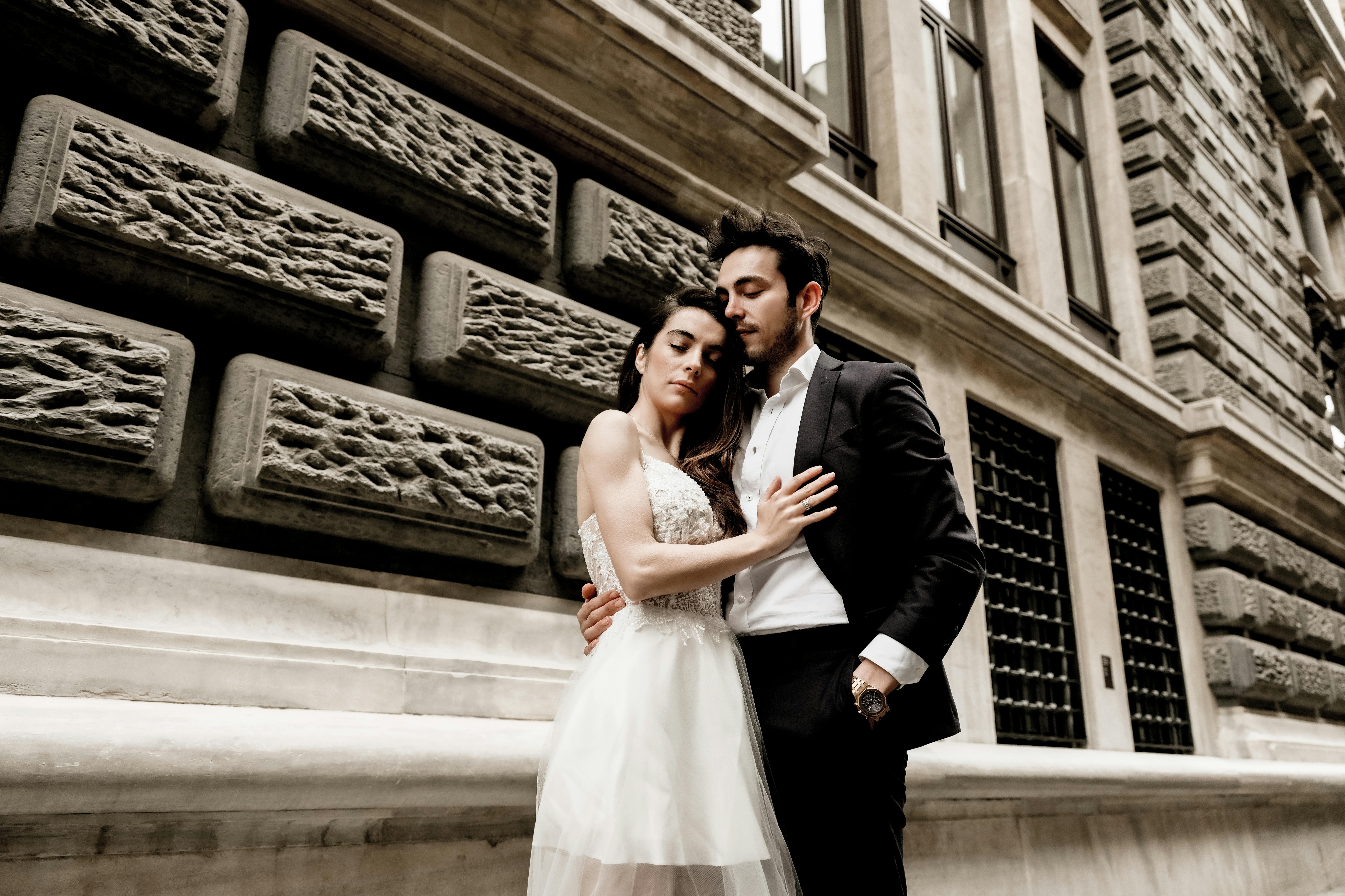 A stylish couple in wedding attire embracing in an urban setting, showcasing elegance and love.