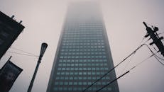 一座高耸的摩天大楼笼罩在雾气中，与布满电线的城市环境相映衬