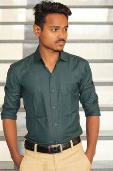 Portrait of a young man in formal attire standing on indoor stairs.
