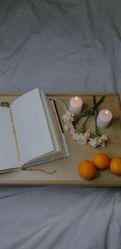 Top view of a cozy reading setup with candles, flowers, and oranges on a bed.