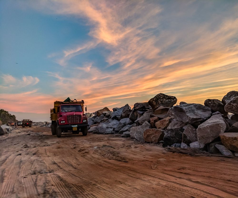 Dump truck hauling on a quarry road beneath a sunset sky