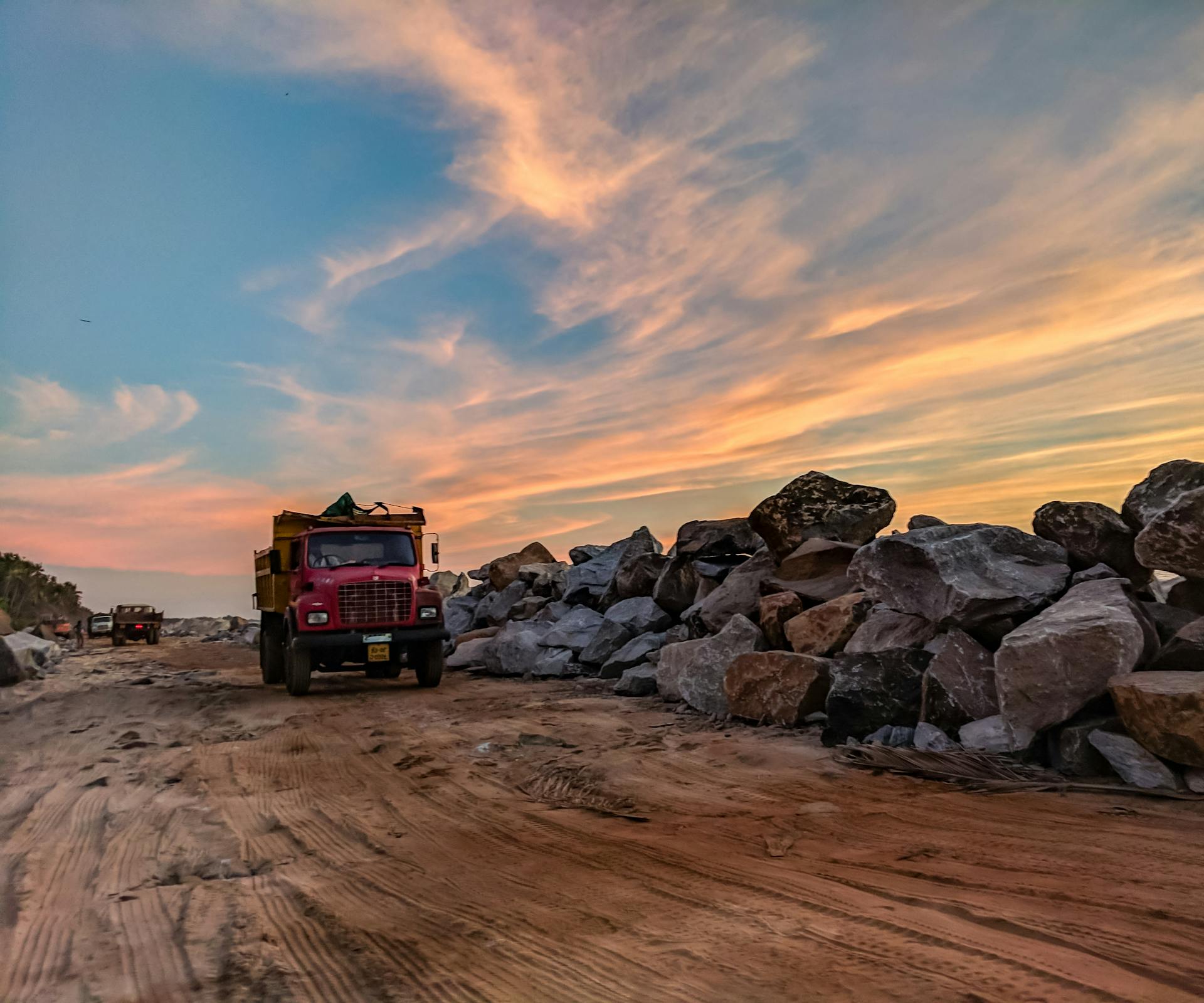 Red Dump Truck Near Filed Rocks Under Cloudy Sky