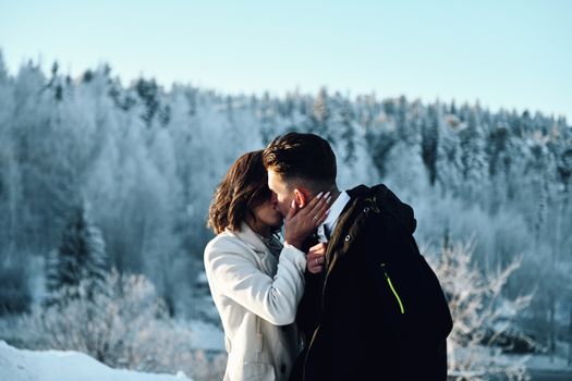 A loving couple shares a kiss in a serene snow-covered forest during winter.