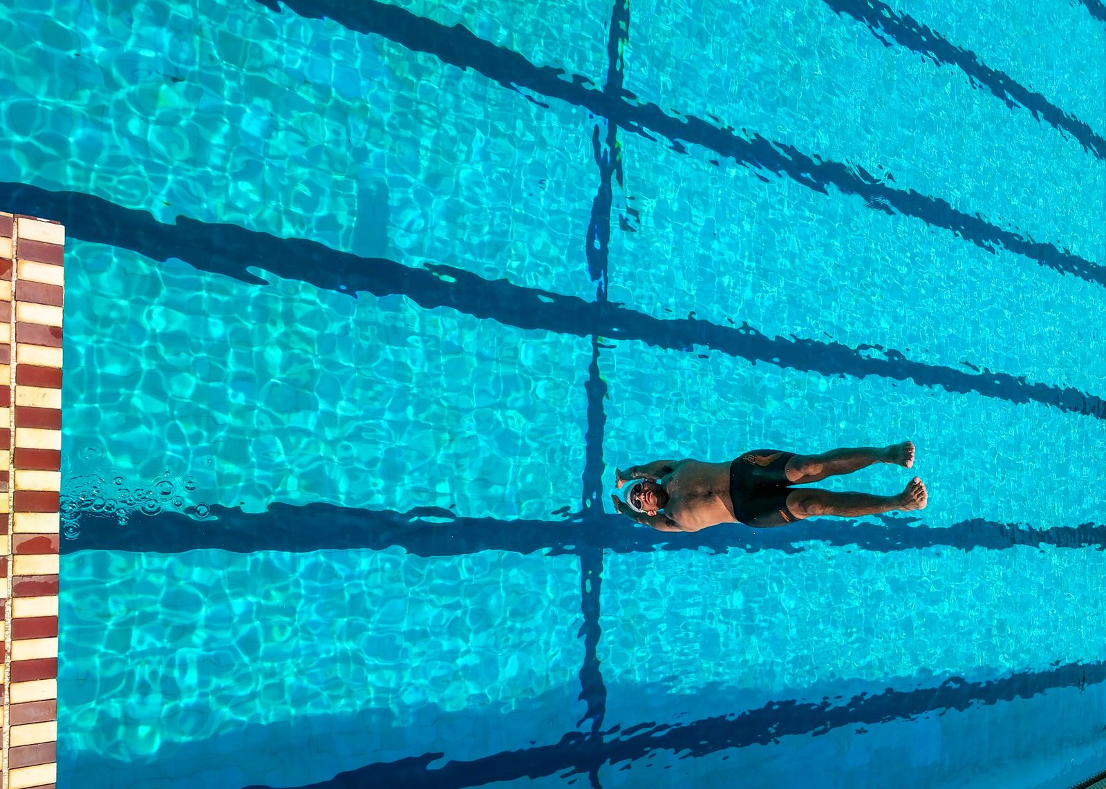 A swimmer doing lengths between dark lane lines, seen from above