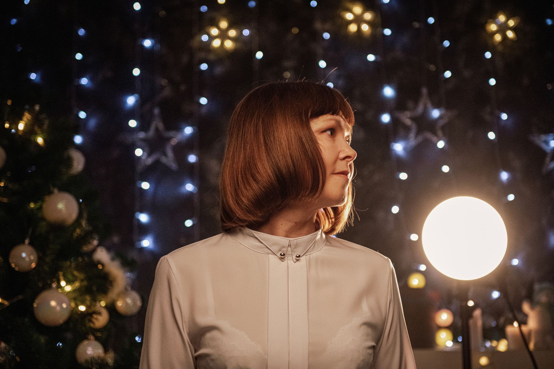 Woman with bob haircut in festive setting with holiday lights and decor.