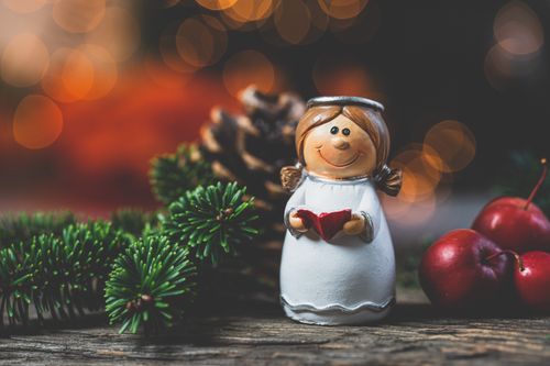 Free Christmas angel figurine amidst holiday decor with fir branches and red apples, creating a festive atmosphere. Stock Photo