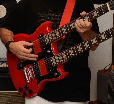 Close-up of a musician playing a double neck electric guitar indoors.