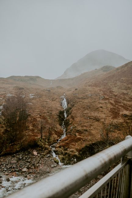Foggy Scottish Highlands landscape featuring a cascading waterfall and rugged terrain.
