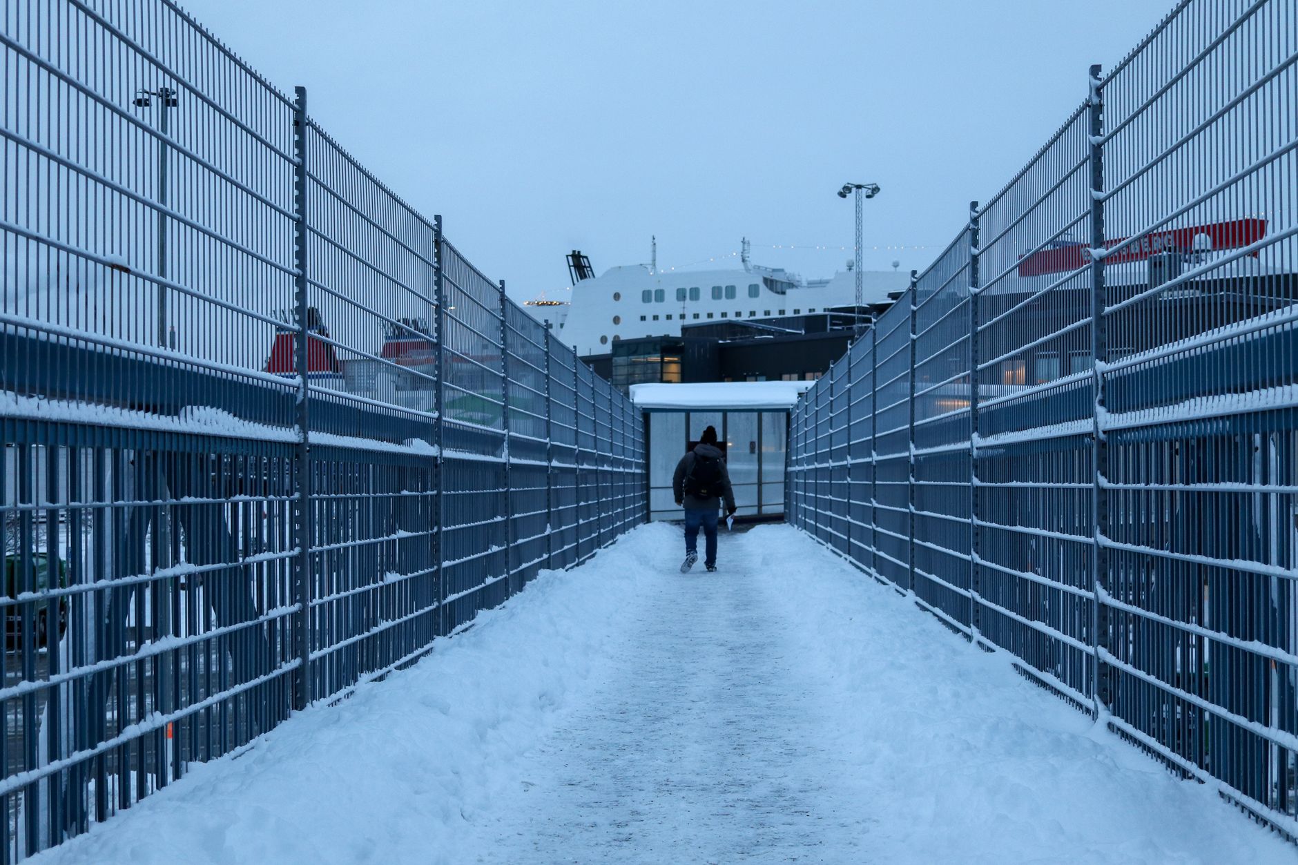 Person walking on snow-covered bridge towards ferry, highlighting winter travel.