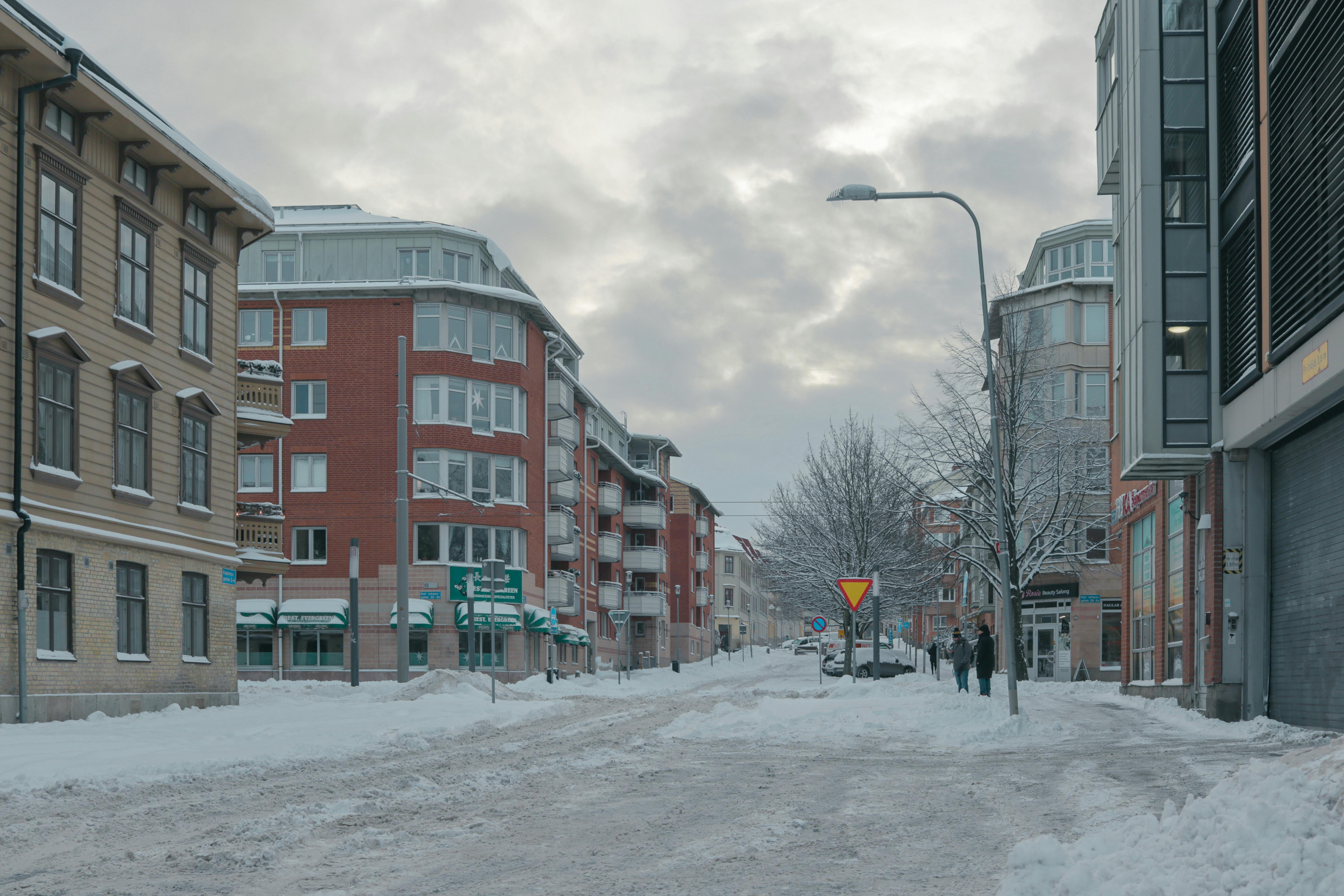 Winter street scene in Göteborg, Sweden with snow-covered buildings and people walking under cloudy skies.