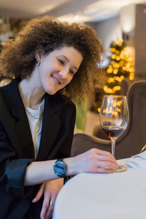 A Woman in Black Blazer Sitting on the Chair while Looking at the Glass of Wine on the Table