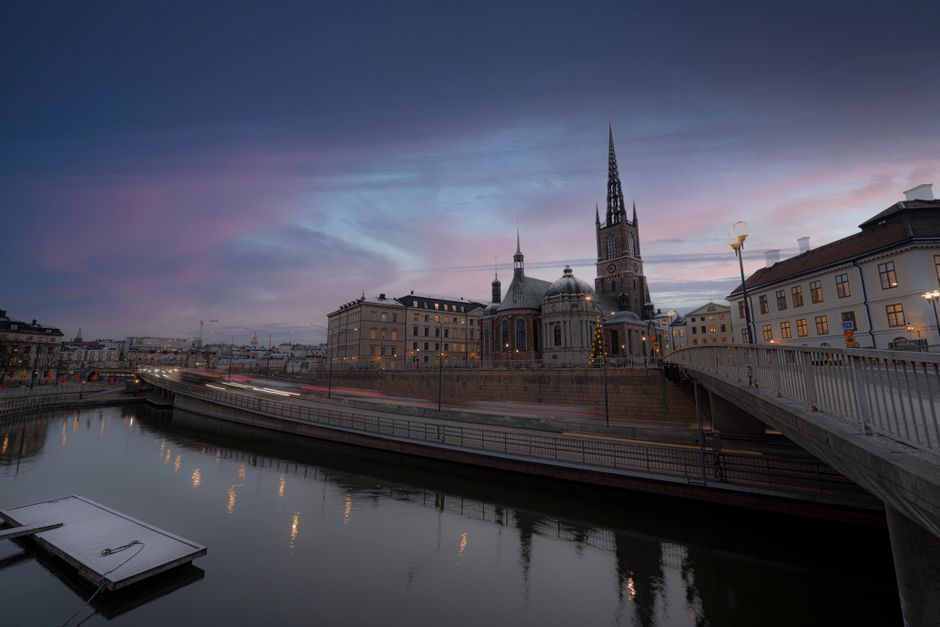 Twilight view of Riddarholmen Church and surrounding architecture in Stockholm, reflecting in calm waters.