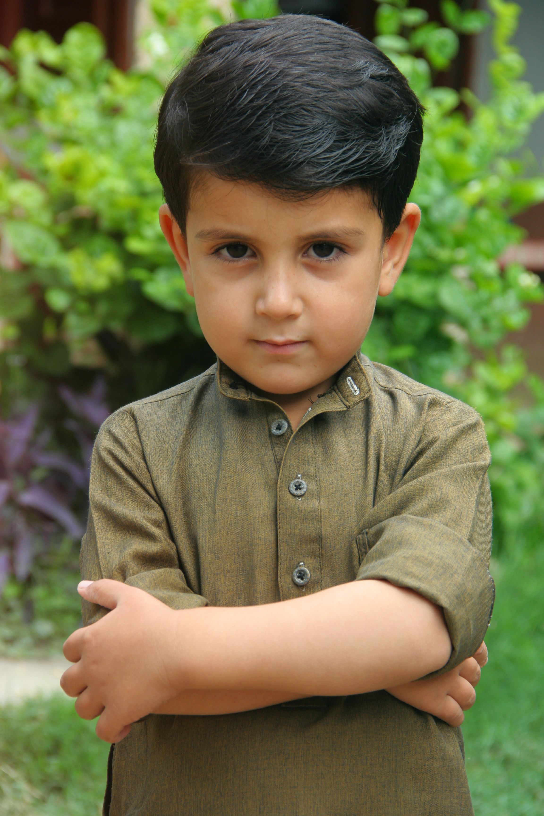 A young boy with a serious expression stands confidently outdoors.