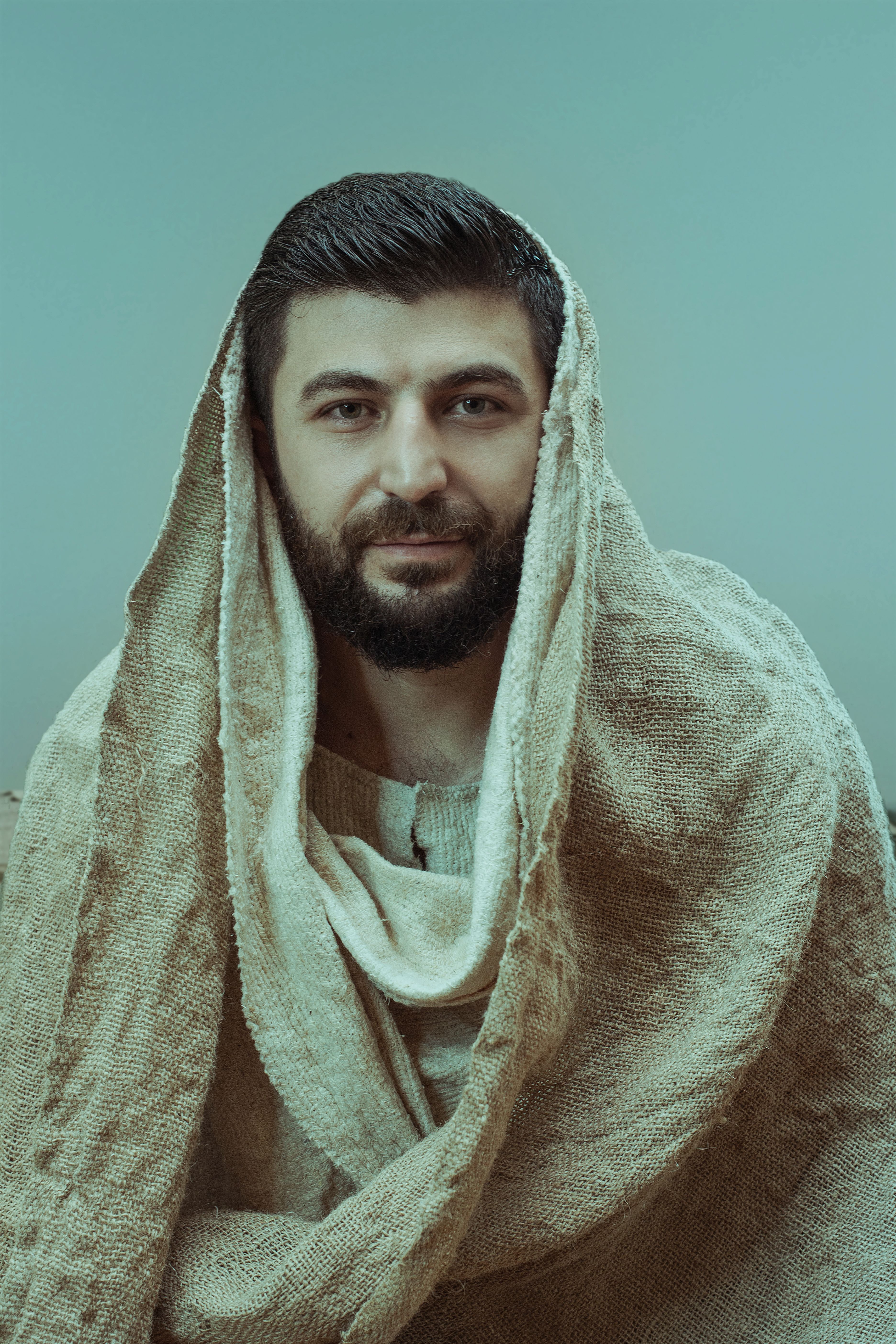 A bearded man with a serene expression wearing traditional attire and headscarf.