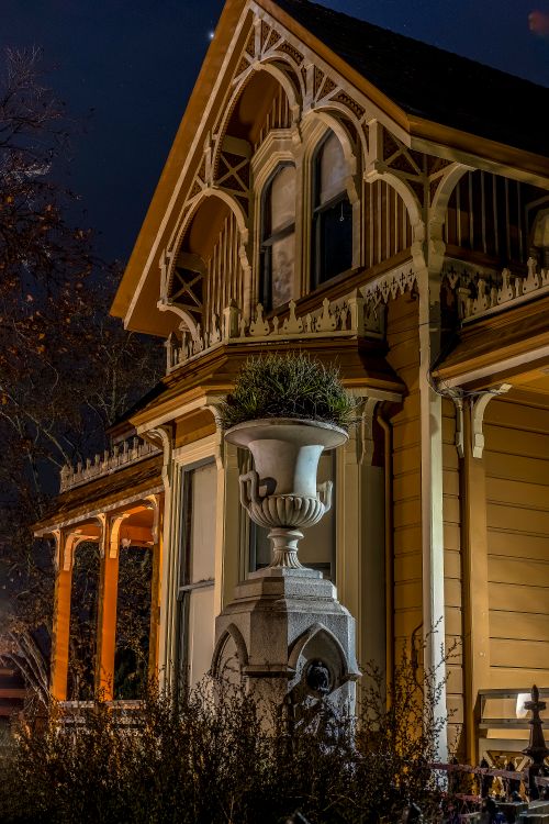 Free Charming Victorian house exterior at night showcasing ornate designs and a grand planter in warm lighting. Stock Photo
