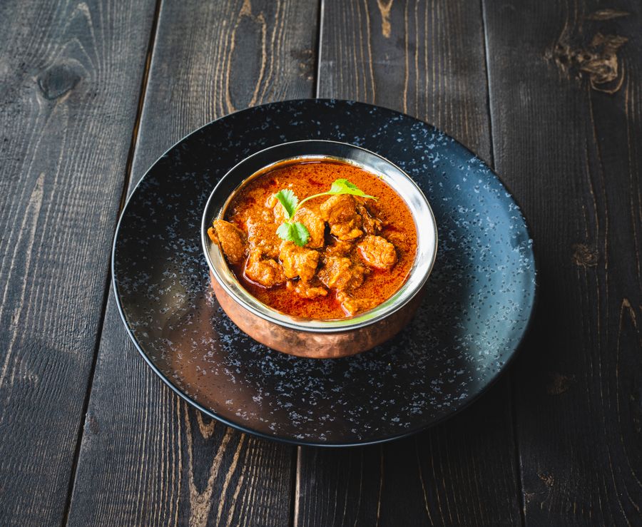 Spicy chicken curry garnished with coriander on a wooden table